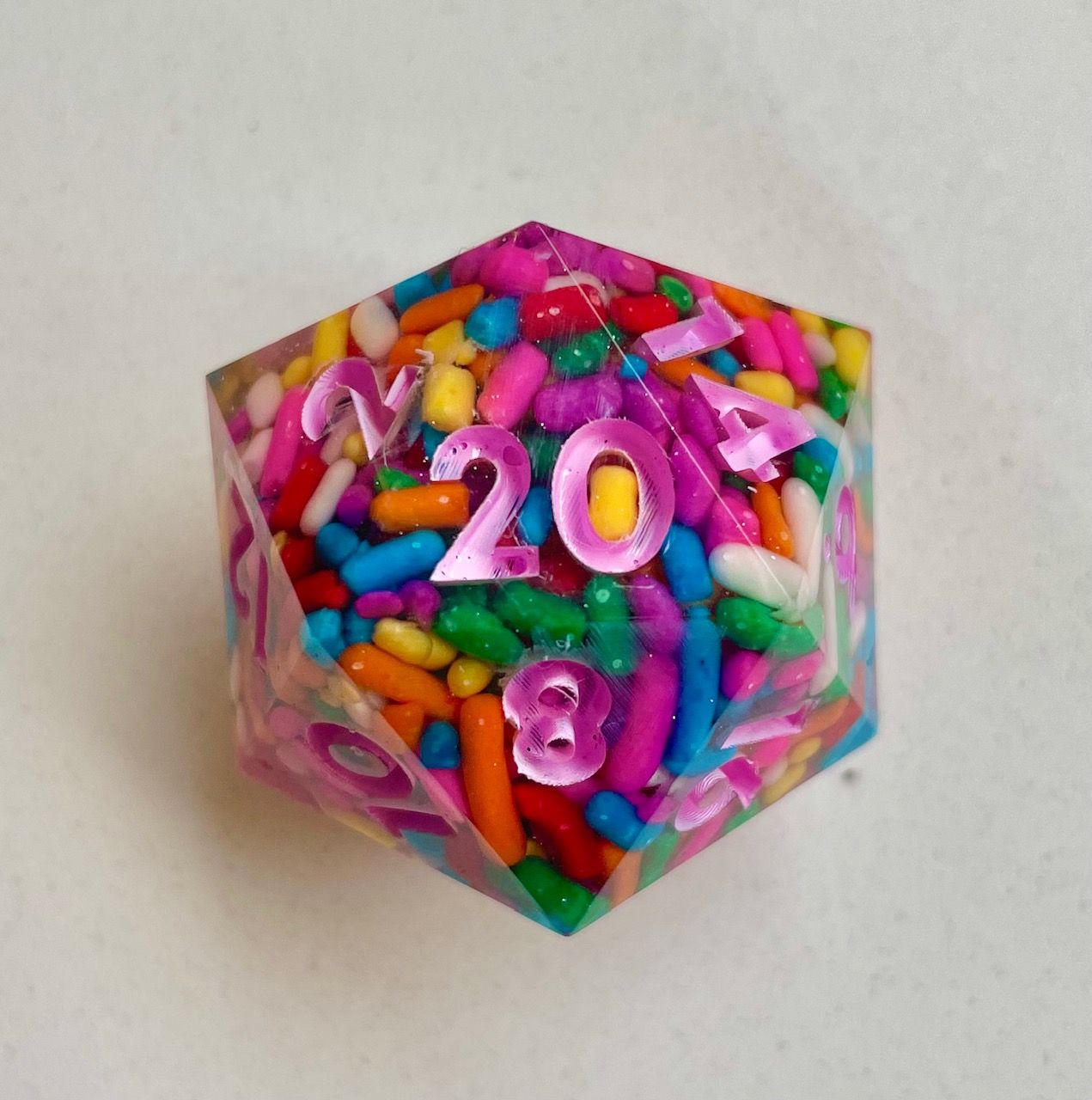 Close-up of a 20 sided die full of colorful sprinkles with pink numbers