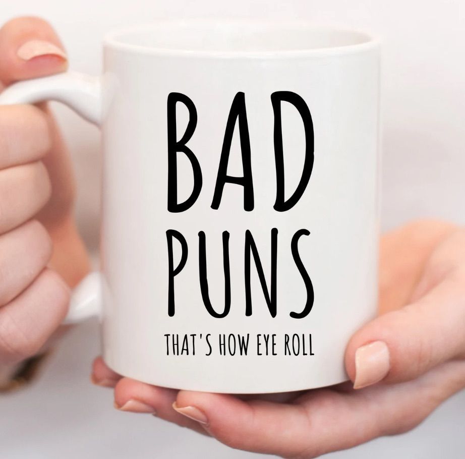 White mug held in white hands. The mug reads "bad puns: that's how eye roll."