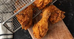four pieces of fried chicken tumbling out of a deep fry basket onto a cutting board