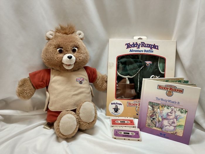 a Teddy Ruxpin doll arranged next to books and cassette tapes