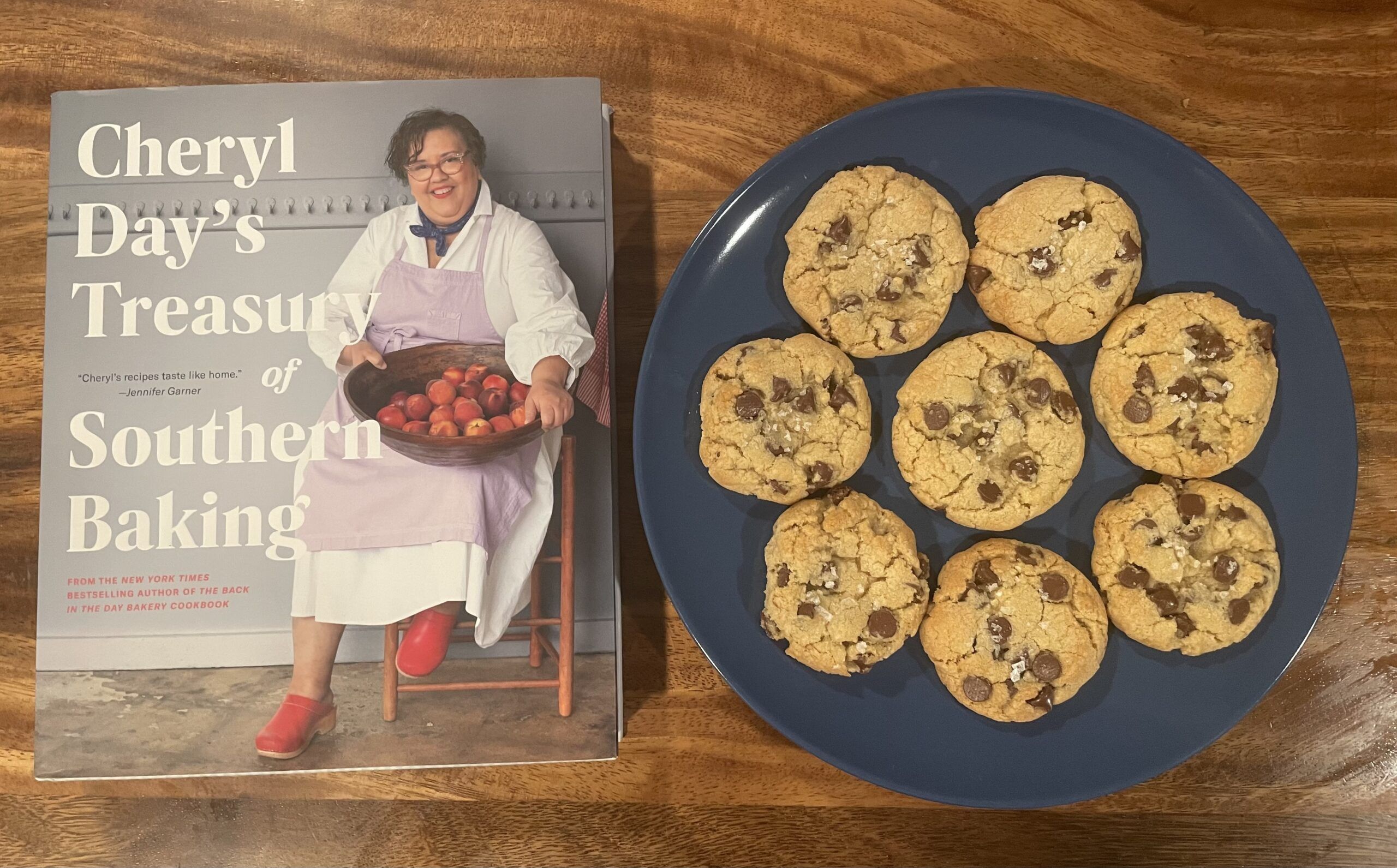 Cheryl Day's Treasury of Southern Baking cookbook on a wooden table next to a plate of classic looking chocolate chip cookies sprinkled with flaky salt.