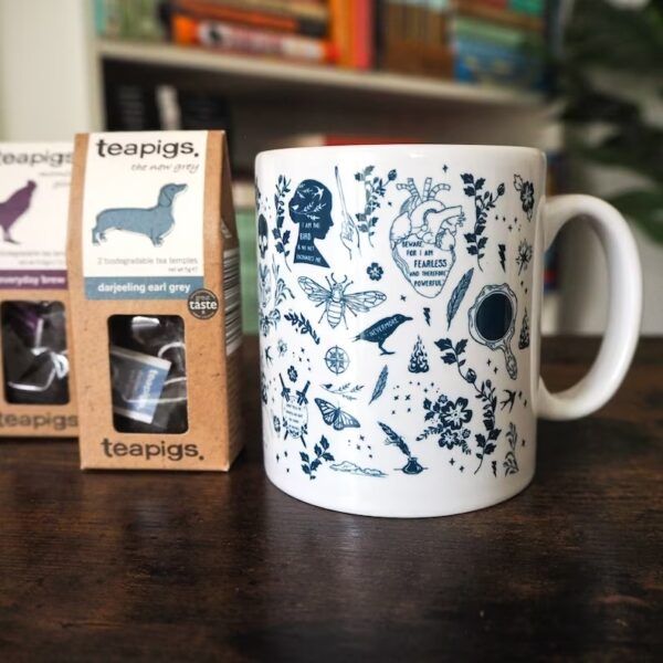 White ceramic mug with literary drawings in blue and tea bags on the side.