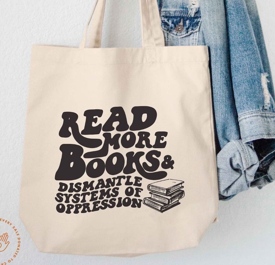 Image of a canvas tote bag with black text that says "read more books & dismantle systems of oppression."