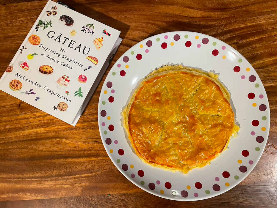 Image of a sad, round, flat pastry on a dotted serving plate next to the cookbook Gateau
