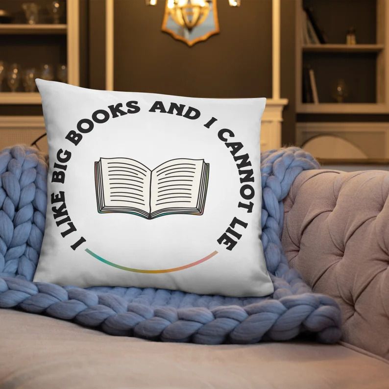 Photo of a white pillow with the text i like big books and I cannot like written in a circle on it, a line with a rainbow colour connecting the beginning and end of the sentence and creating a full circle.