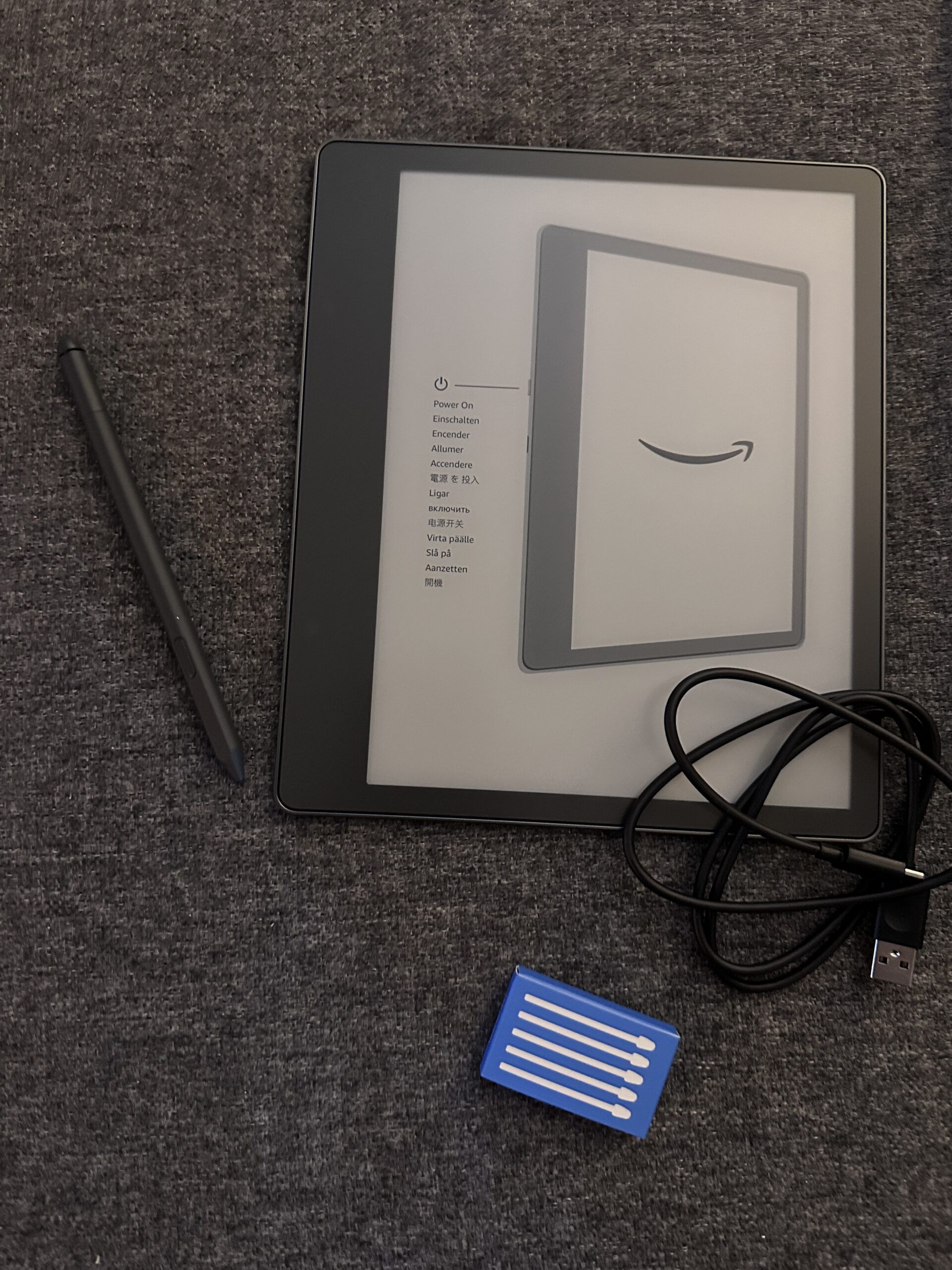 A flat lay of a Kindle pen, a Kindle, a charging cord, and pen tip replacements