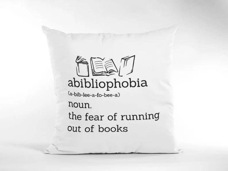 Photo of a white pillow with the print of some drawn books and the words abibliophilia, noun. the fear of running out of books