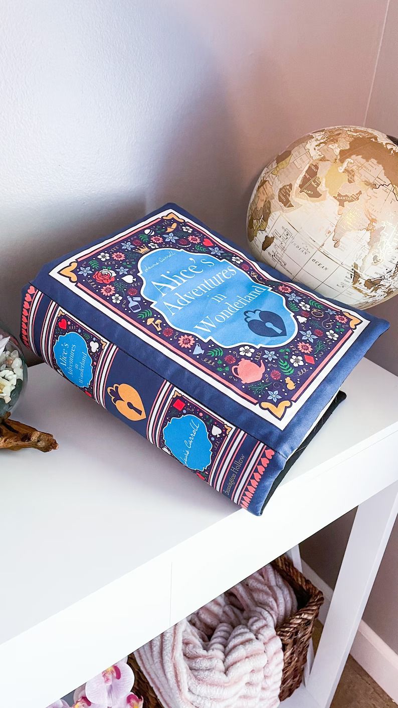 Photo of a pillow shaped like a book with the cover of Alice In Wonderland.