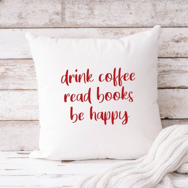 Photo of a white pillow with a text in red saying drink coffee read books be happy