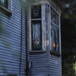 exterior of a wooden house with a lamp without a shade and a rabbit doll seen in a bay window