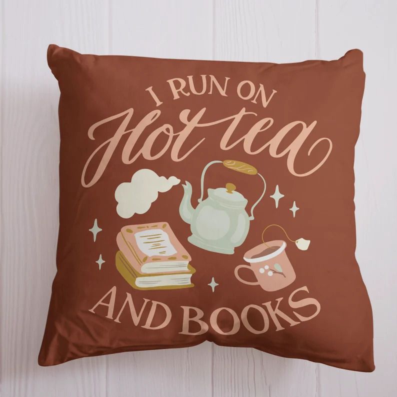 Photo of a brown pillow with pink letters saying I run on hot tea and books with a print of a tea pot, mug and stacked books in pretty pink and light blue colours