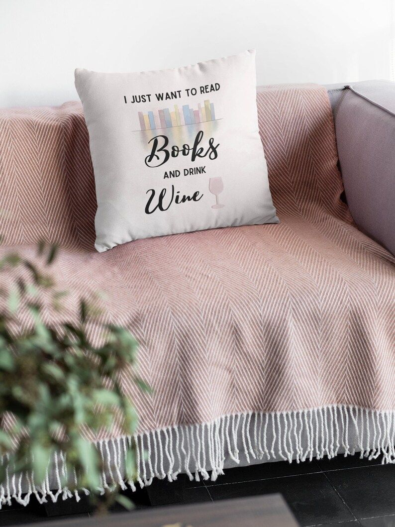 Photo of a white pillow with painted books side by side showing the spines and the text I just want to read books and drink wine, a glass of wine printed on the right side.