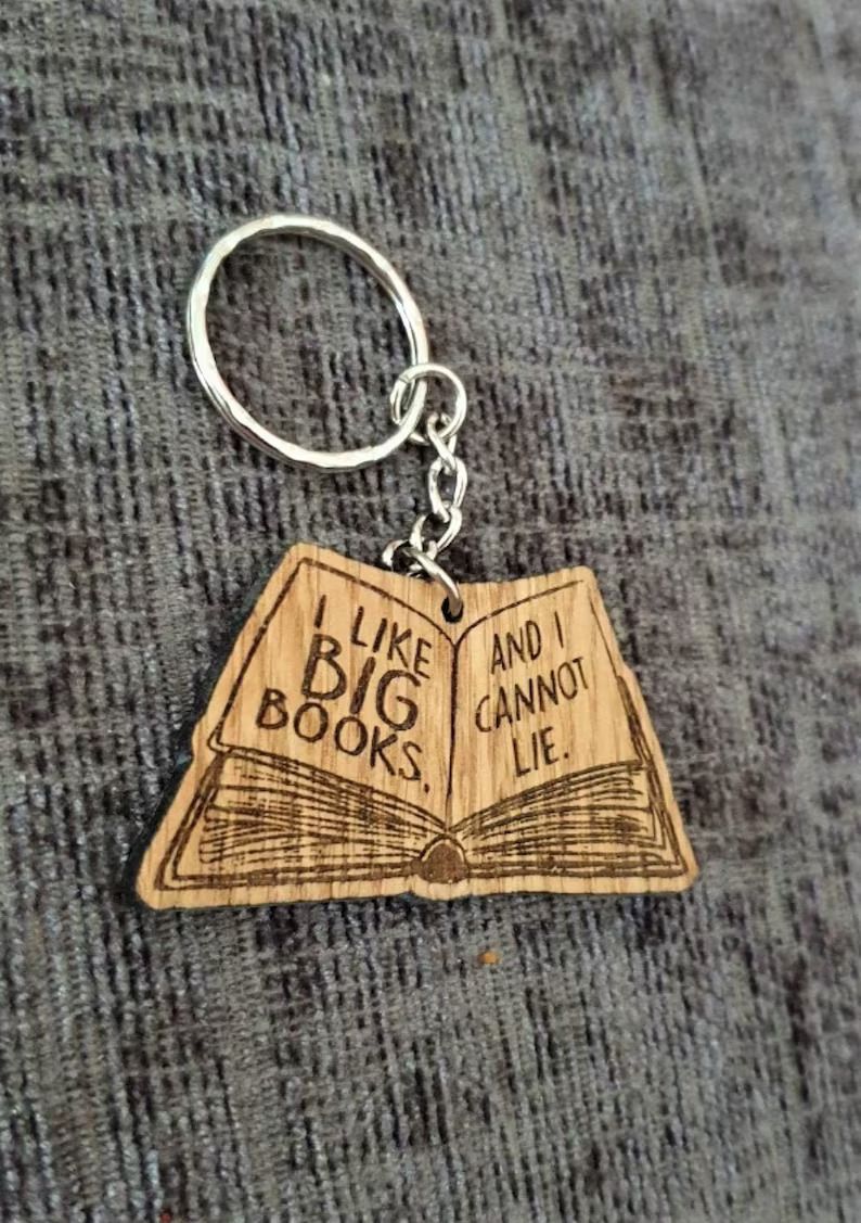 Photo of a wooden keychain with the shape of an open book with the text I like big books and i cannot lie.