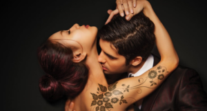 a cropped cover of Hate To Want You, showing an Asian woman with tattoos down one arm. She embracing a man who is kissing her neck.