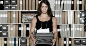 image of white person with type writer in front of bookshelves