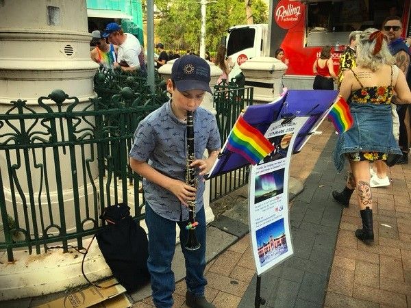 Image of young street performer during Sydney Mardi Gras celebrations. He is playing a clarinet with rainbow flags attached to his music stand. Permission to use photo given by his parents. 