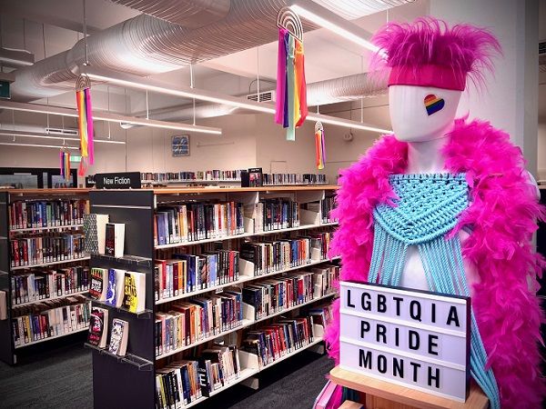 Image of Waverley Library, with display of mannequin with pink boa, pink fluffy hat, and blue crochet top. There is a sign that says "LGBTQIA PRIDE MONTH". It stands next to library shelves with books as display for Sydney WorldPride 2023