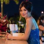a still of Gemma Chan as Astrid in Crazy Rich Asians. She is dressed up andsitting at an outdoor bar.