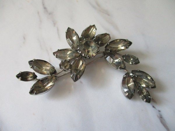A brooch that looks somewhat floral made of grayish crystal.