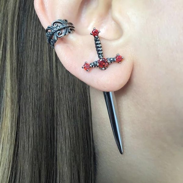 Sword-shaped earrings that go through the ear, embellished with red stones. 