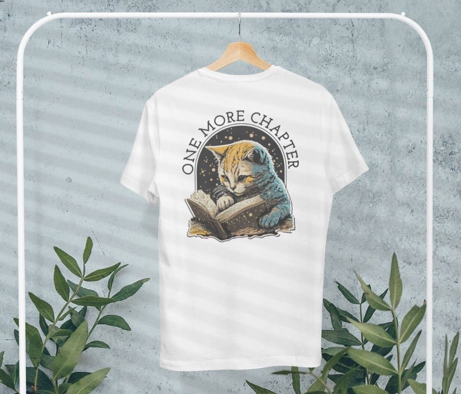 Image of a white shirt featuring a cat reading a big book. It says "one more chapter."