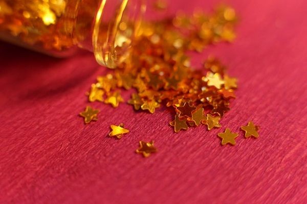 Gold star confetti spilling out from a glass jar over a red surface