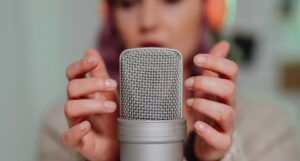 fair skinned woman with purple hair lightly taps on a microphone