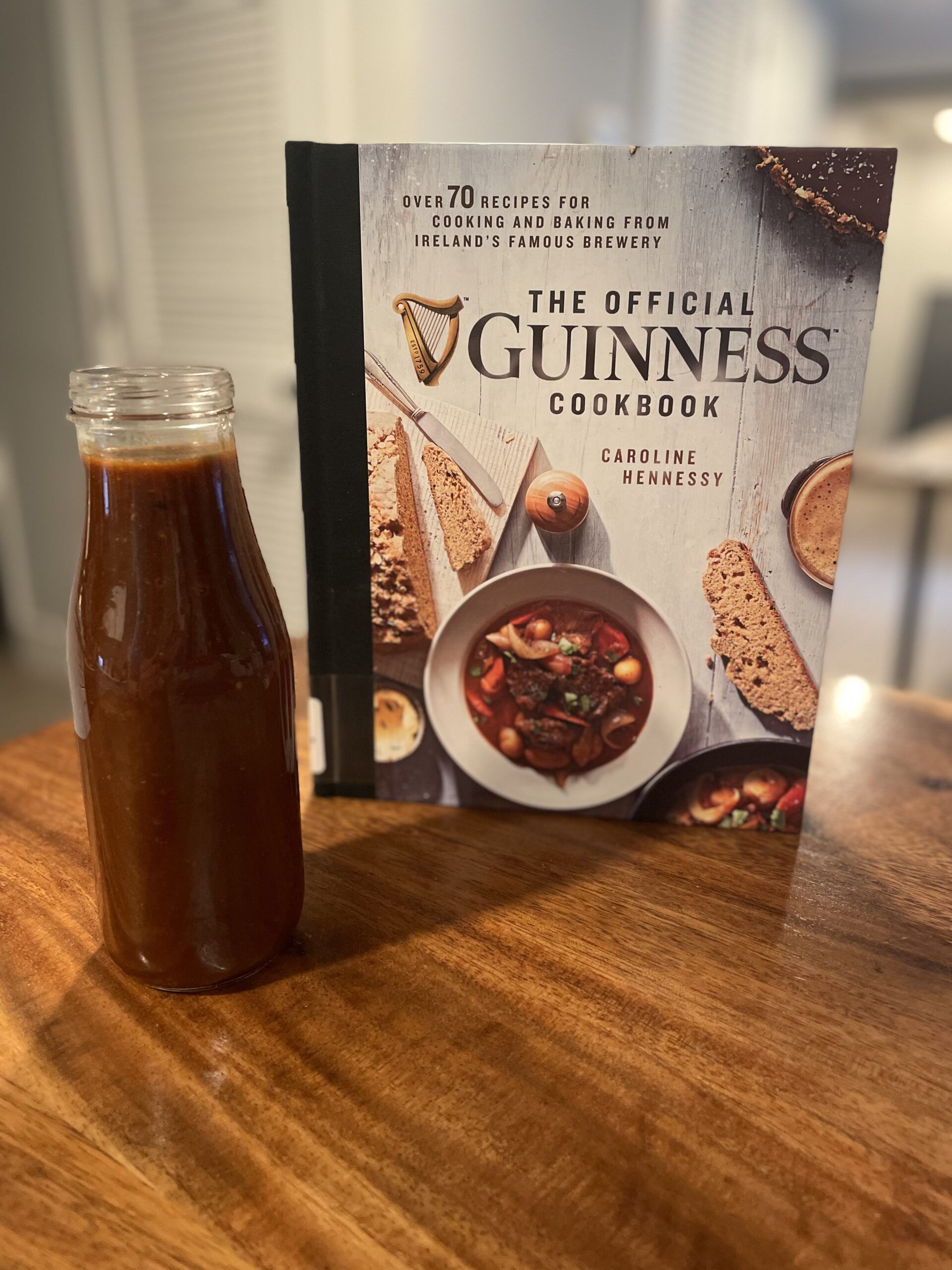 Image of The Official Guinness Cookbook next to a tall glass jar of dark brownish red BBQ sauce