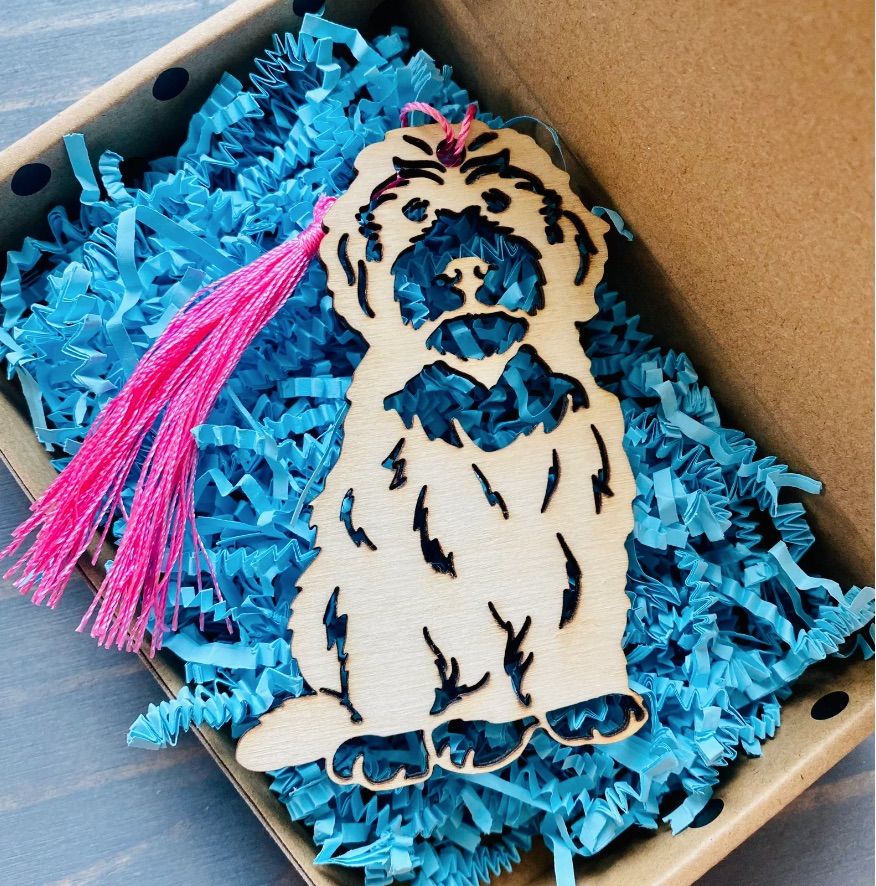 Image of a wooden Doodle dog bookmark. It is inside a box with blue tissue. 