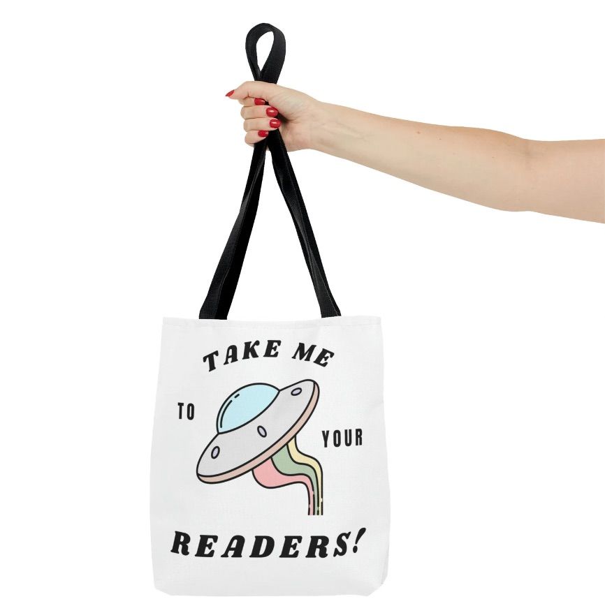 Image of a white tote bag being held by a white hand with red fingernails. The tote has a space ship and says "take me to your readers!"