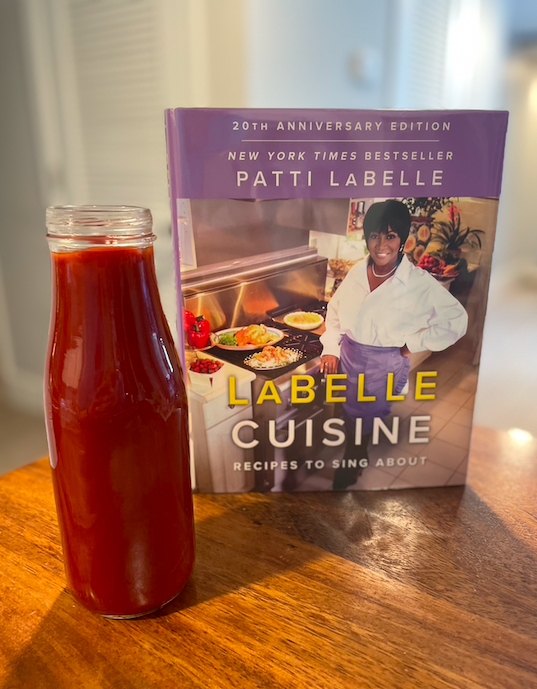 Photo of the cookbook LaBelle Cuisine next to a tall glass jar of bright red BBQ sauce