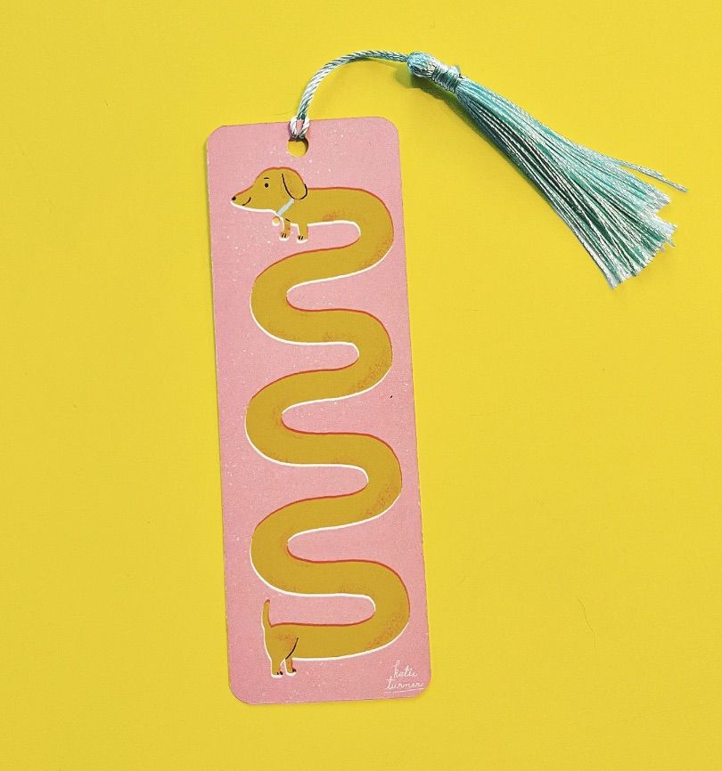 Image of a pink bookmark featuring a brown weiner dog. 