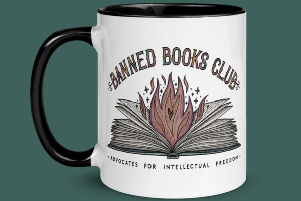 White coffee mug with black handle and an illustration of an open book with a fire in between the pages and the text "Banned Books Club. Advocates for Intellectual Freedom."