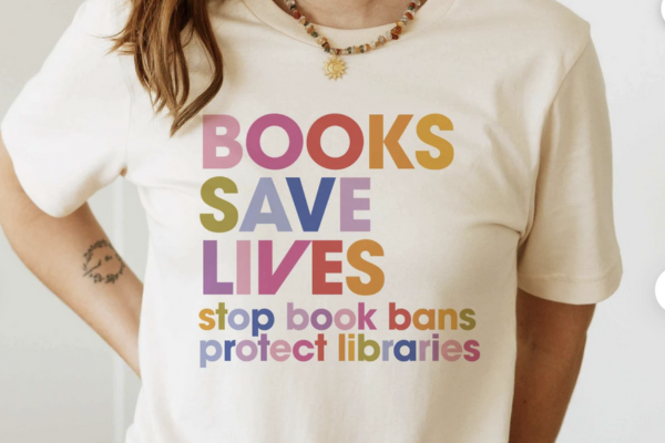White tee shift with colorful rainbow text that reads "Books save lives. Stop book bans. Protect libraries."