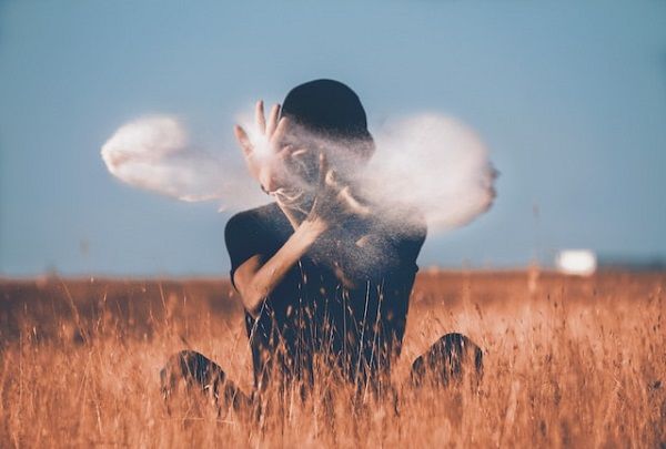 Person sitting in a field waving their hands in front of their face with magical dust