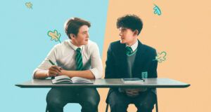 a promotional image of Heartstopper showing Nick and Charlie sitting at desks and smiling at each other, with leaf illustrations falling around them