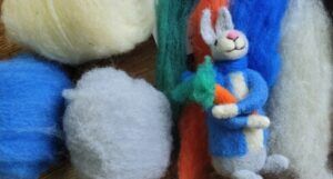 a felt iPeter Rabbit holding a carrot positioned next to several balls of felt