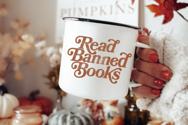 White campfire mug with red, curly text reading "read banned books"