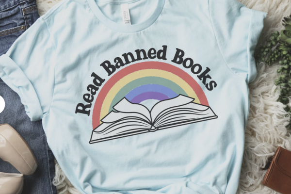 Light blue shirt featuring an open book with a rainbow behind it and the text "read banned books"