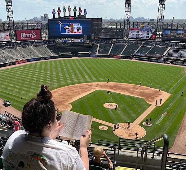 a woman reading a book in a seat that overlooks a ballpark