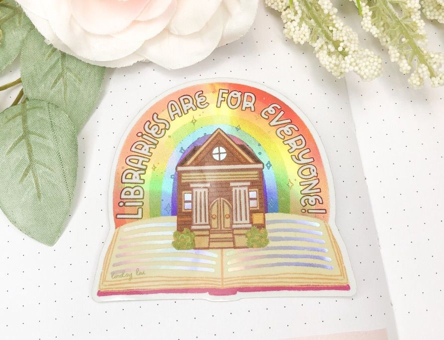 Image of a holographic sticker featuring an open book and library on top of it. 