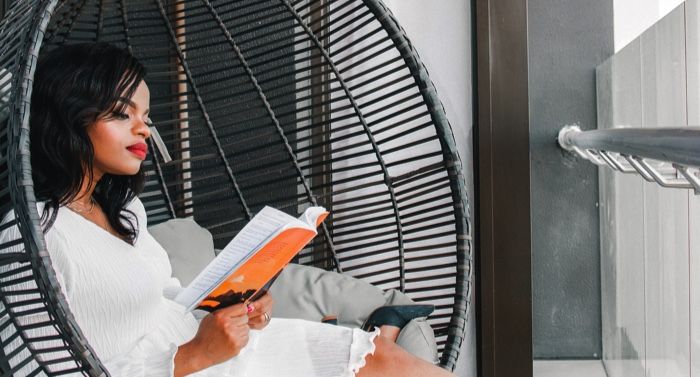 brown-skinned Black woman reading a book in a hanging wicker chair