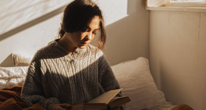 lighter-skinned woman readnig a book while a sunbeam shines on her