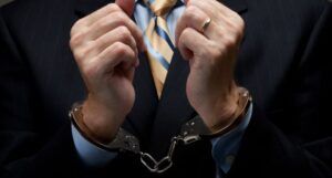 a white man wearing a suit. His wrists are handcuffed