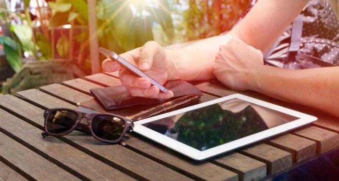 Image of a tablet and sunglasses on a table, with a hand holding a cell phone