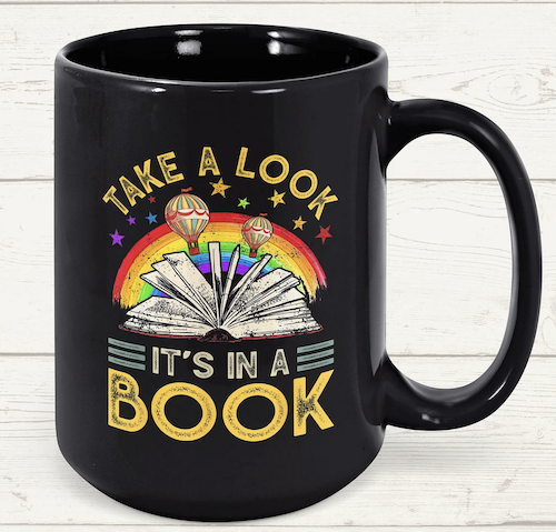 black mug with illustration of book and rainbow that says take a look it's in a book