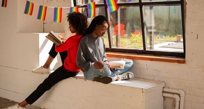 two black women reading books; rainbow flag in the back