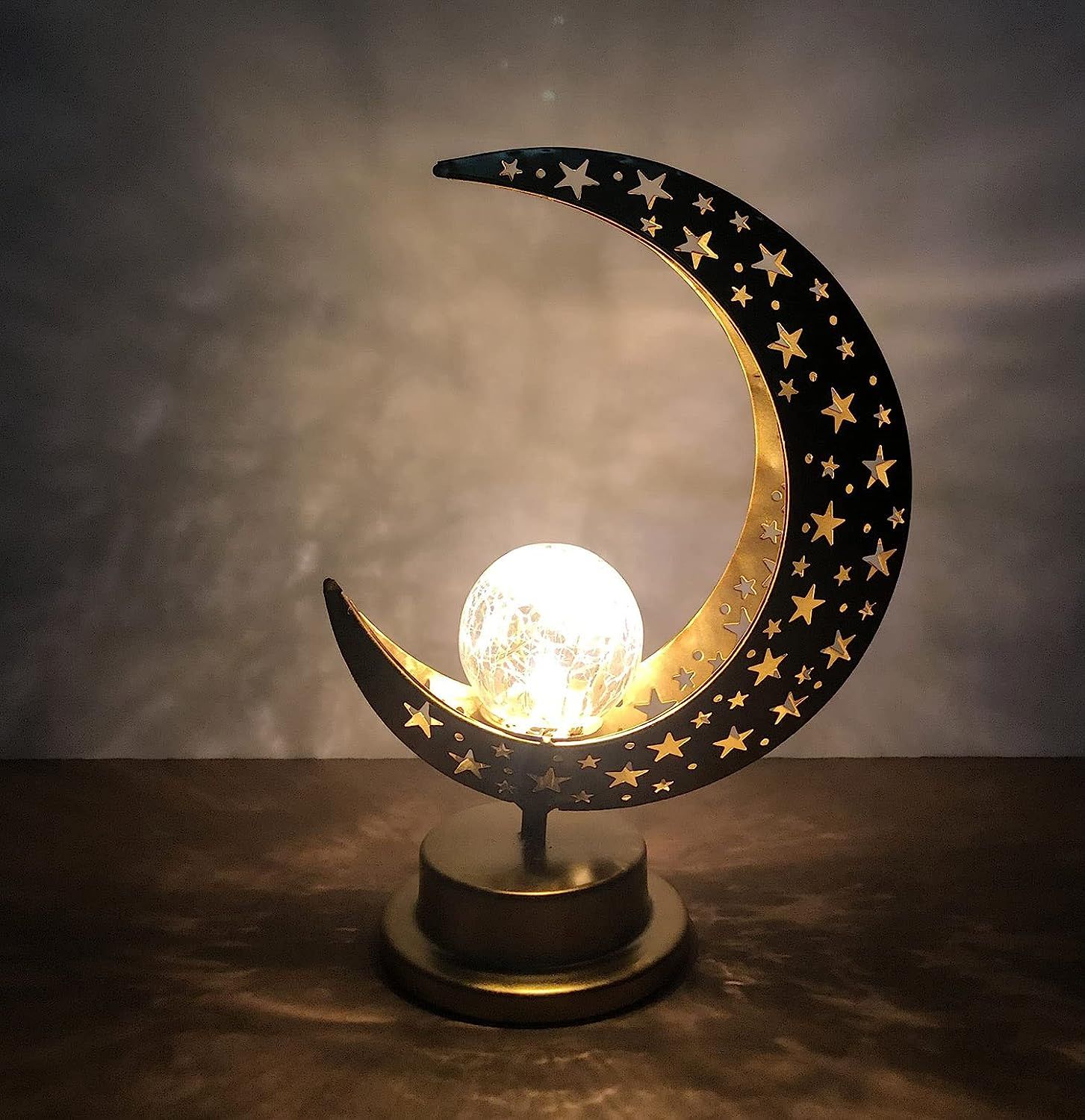 A crescent moon shaped cut tin lamp with tiny stars all over it, and a round ball filled with string lights resting in the lower curve 