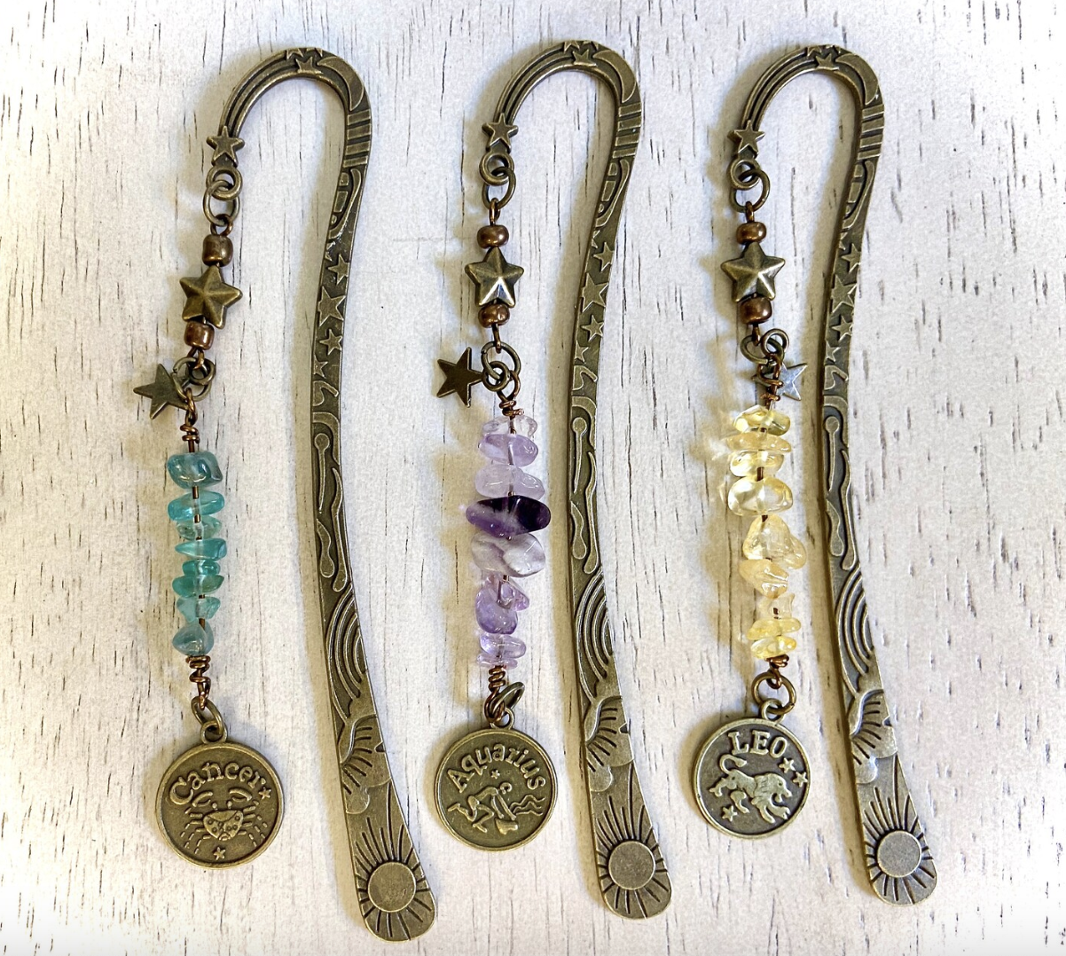 Three thin bronze bookmarks with tassels with crystal beads and a token on the end with different zodiac signs