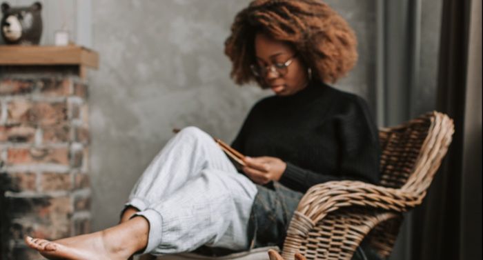 brown skinned black woman with blond afro reading in a chair